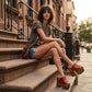 Close-up image of a model from the waist down wearing the Red Luxury Queen Sandals by Sol Caleyo and rolled-up dark denim jeans, posing on a classic brownstone stone staircase in New York City.