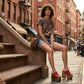 Close-up image of a model from the waist down wearing the Red Luxury Queen Sandals by Sol Caleyo and rolled-up dark denim jeans, posing on a classic brownstone stone staircase in New York City.