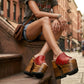 Close-up image of a model from the waist down wearing the Red Luxury Queen Sandals by Sol Caleyo and rolled-up dark denim jeans, posing on a classic brownstone stone staircase in New York City.