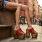 Close-up image of a model from the waist down wearing the Red Luxury Queen Sandals by Sol Caleyo and rolled-up dark denim jeans, posing on a classic brownstone stone staircase in New York City.