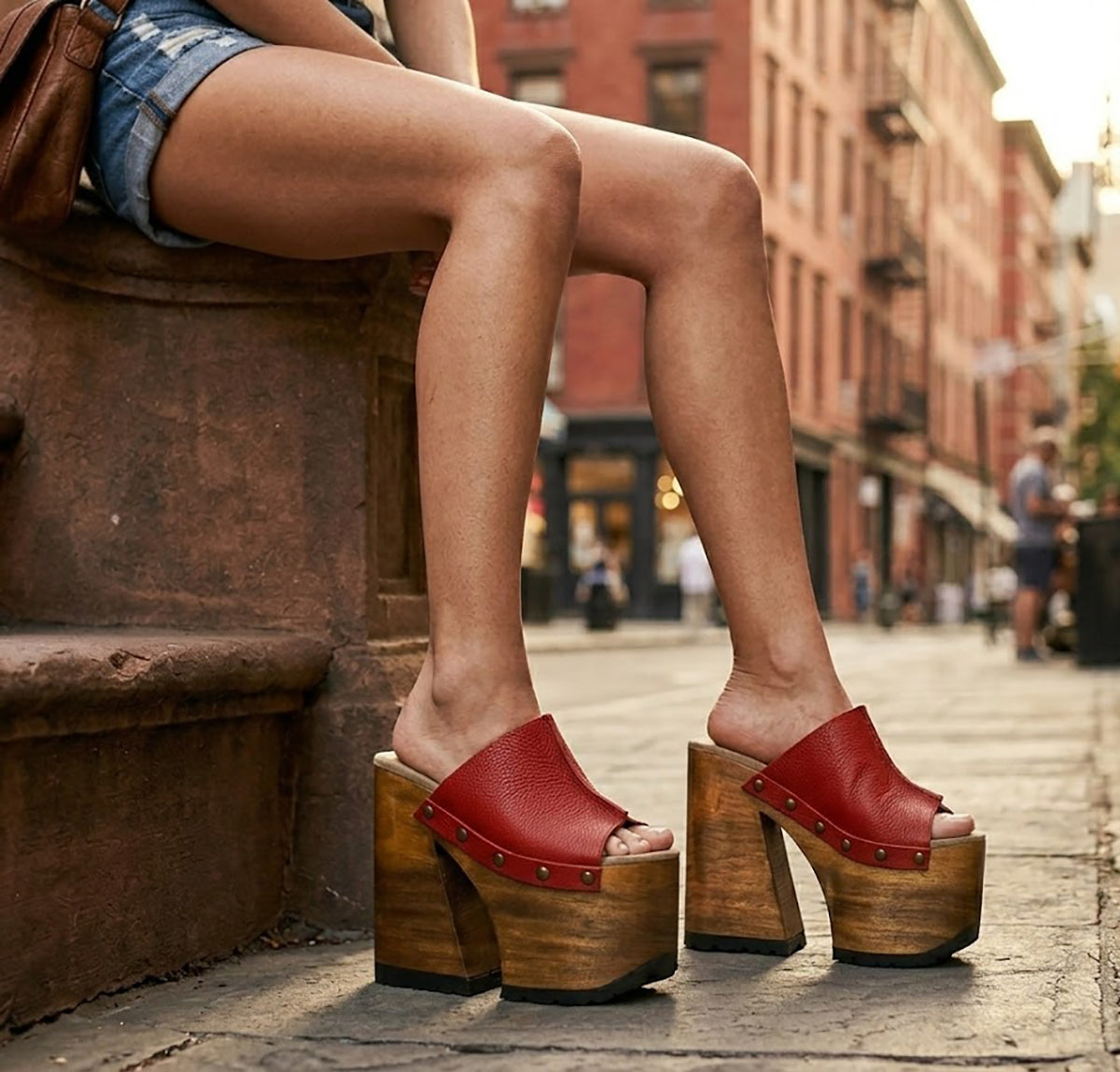Close-up image of a model from the waist down wearing the Red Luxury Queen Sandals by Sol Caleyo and rolled-up dark denim jeans, posing on a classic brownstone stone staircase in New York City.