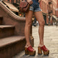 Close-up image of a model from the waist down wearing the Red Luxury Queen Sandals by Sol Caleyo and rolled-up dark denim jeans, posing on a classic brownstone stone staircase in New York City.