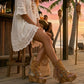 Boho-chic model wearing Atenea Camel suede platform boots at a beach chiringuito, showcasing the warm earthy tones and artisanal fringe details in a relaxed coastal summer atmosphere.