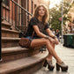Model walking in New York City wearing the exotic Tokio Snake Clogs by Sol Caleyo, showcasing the python-print leather and high wenge platform against an urban brownstone backdrop.