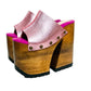Side view of Sol Caleyo Pink Luxury Queen Sandals featuring metallic pink leather, bronze studs, and a high architectural wooden platform heel against a white background.
