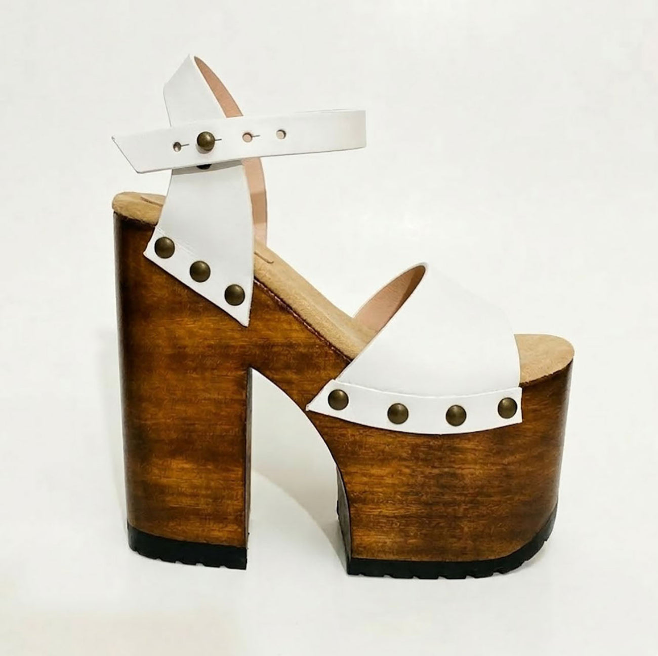 Side view of Crazy White Sandals by Sol Caleyo, featuring white leather straps with bronze studs on a high dark wood platform and tractor sole.
