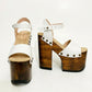 Side view of Crazy White Sandals by Sol Caleyo, featuring white leather straps with bronze studs on a high dark wood platform and tractor sole.