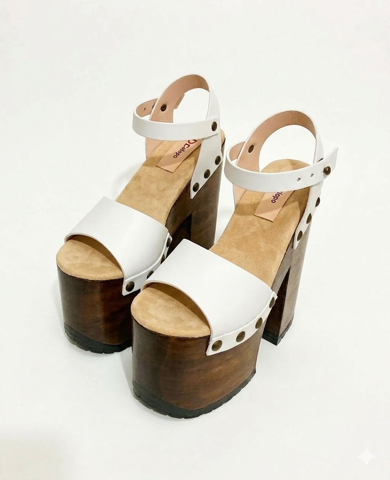 Side view of Crazy White Sandals by Sol Caleyo, featuring white leather straps with bronze studs on a high dark wood platform and tractor sole.