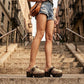 Fashion model wearing Sol Caleyo Route 66 snake print platform clogs with denim shorts and a vintage t-shirt on city steps.