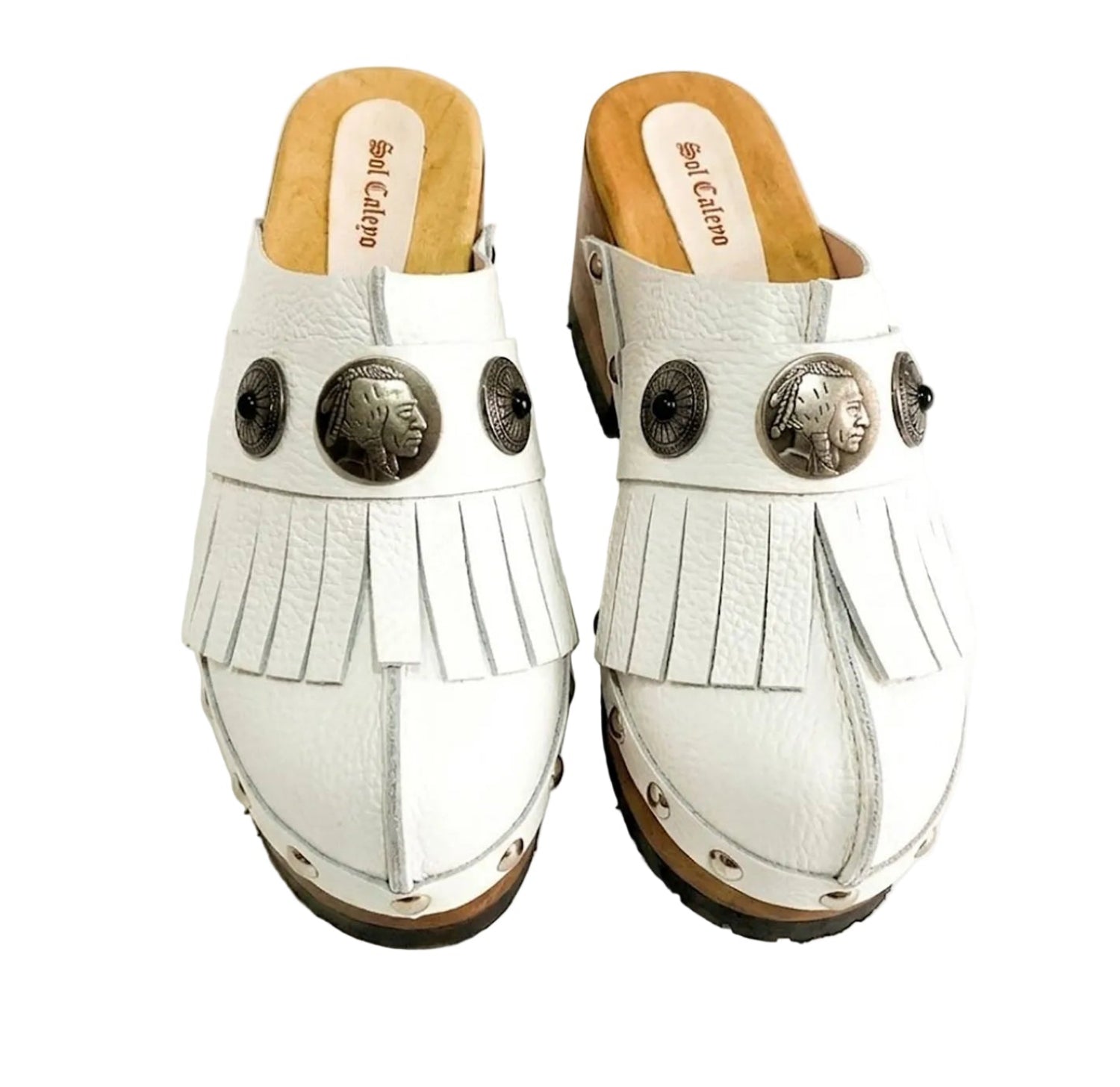 Top view of a pair of handmade white textured full-grain leather clogs with leather fringes and detailed Native American chief profile metal conchos on a wooden platform.