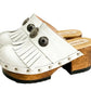 Top view of a pair of handmade white textured full-grain leather clogs with leather fringes and detailed Native American chief profile metal conchos on a wooden platform.