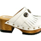 Top view of a pair of handmade white textured full-grain leather clogs with leather fringes and detailed Native American chief profile metal conchos on a wooden platform.