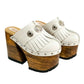 Side view of White Indian Clogs XL featuring extreme 17cm natural wood platform, white leather fringes, and antique silver metal conchos.
