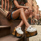 Close-up of a model wearing Sol Caleyo White Indian Clogs XL with 17cm heels and metal conchos, styled with denim shorts in an urban setting.