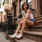 Close-up of a model wearing Sol Caleyo White Indian Clogs XL with 17cm heels and metal conchos, styled with denim shorts in an urban setting.