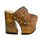 Side profile of Sol Caleyo Light Brown Indian Clogs XL featuring a high 17cm wooden platform, textured brown leather, decorative fringes, and antique metal conchos on a white background.