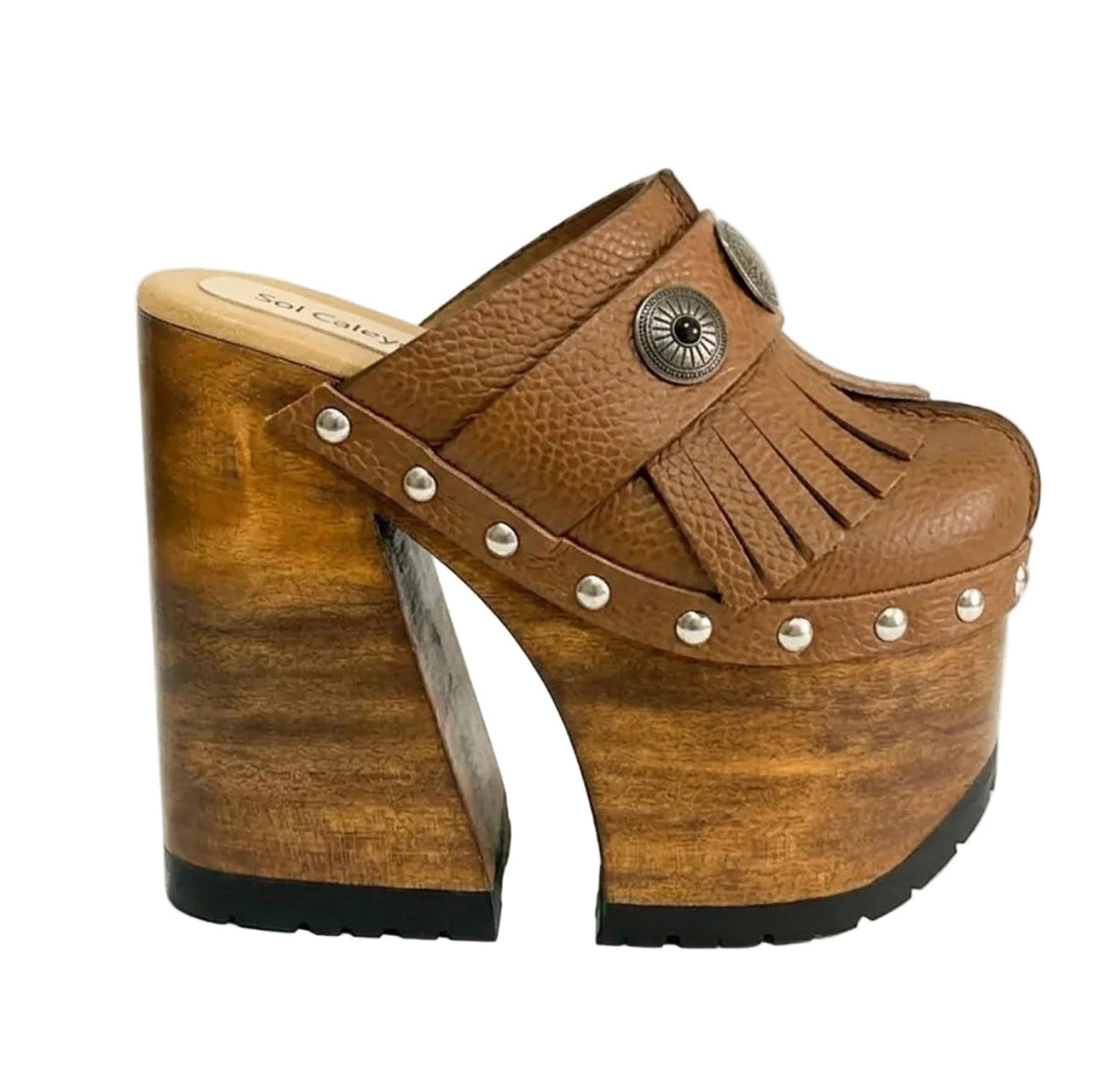 Side profile of Sol Caleyo Light Brown Indian Clogs XL featuring a high 17cm wooden platform, textured brown leather, decorative fringes, and antique metal conchos on a white background.