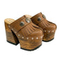 Side profile of Sol Caleyo Light Brown Indian Clogs XL featuring a high 17cm wooden platform, textured brown leather, decorative fringes, and antique metal conchos on a white background.