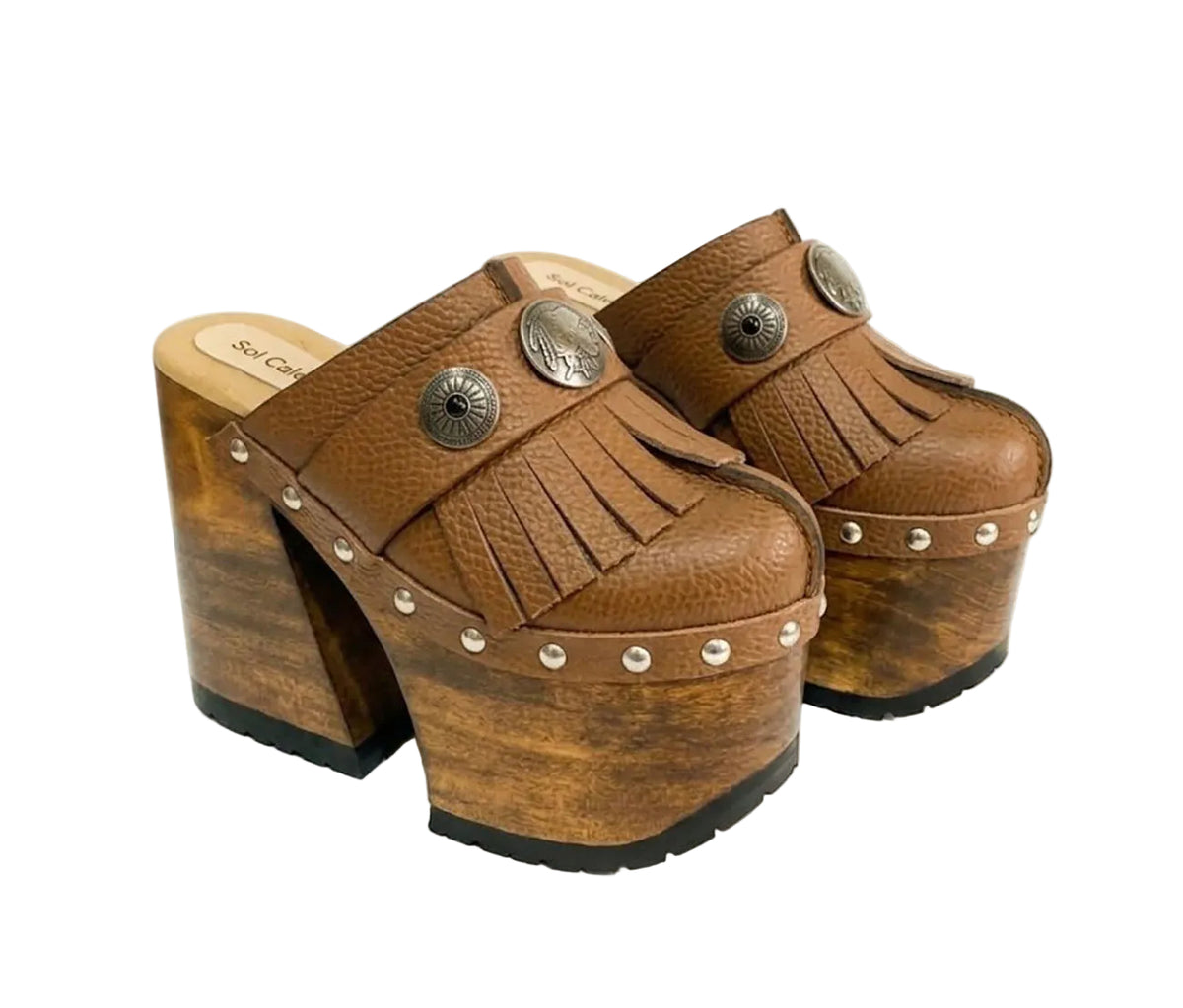 Side profile of Sol Caleyo Light Brown Indian Clogs XL featuring a high 17cm wooden platform, textured brown leather, decorative fringes, and antique metal conchos on a white background.