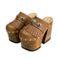 Side profile of Sol Caleyo Light Brown Indian Clogs XL featuring a high 17cm wooden platform, textured brown leather, decorative fringes, and antique metal conchos on a white background.