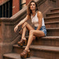 Fashion model sitting on urban brownstone steps wearing Light Brown Indian Clogs XL with denim shorts and a white tank top, showcasing the extreme wooden platform height.