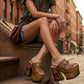 Fashion model sitting on urban brownstone steps wearing Light Brown Indian Clogs XL with denim shorts and a white tank top, showcasing the extreme wooden platform height.