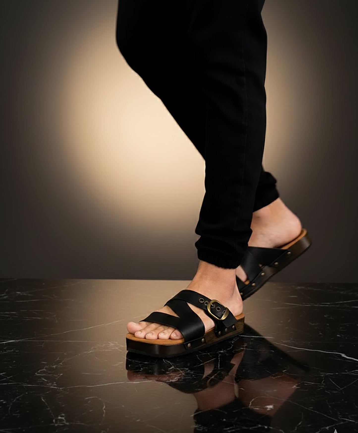 Man wearing handmade black leather wooden sole sandals outdoors, showing fit and rugged style.