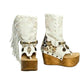 Atenea White Flip Flop Boots by Sol Caleyo, featuring premium white suede, bohemian fringe, shell decorations, and a chunky wooden platform heel against a white background.