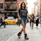 Model sitting on city stairs wearing Sol Caleyo Texas Boots: black leather flip-flop platform sandals with silver studs and chains. Handcrafted 9 cm wooden wedge with a rugged biker aesthetic.