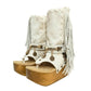 Atenea White Flip Flop Boots by Sol Caleyo, featuring premium white suede, bohemian fringe, shell decorations, and a chunky wooden platform heel against a white background.