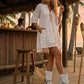 Boho-chic model at a beach club wearing Atenea White suede platform boots, showcasing the white fringe and artisanal details in a sunny, seaside atmosphere.