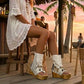 Boho-chic model at a beach club wearing Atenea White suede platform boots, showcasing the white fringe and artisanal details in a sunny, seaside atmosphere.