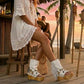 Boho-chic model at a beach club wearing Atenea White suede platform boots, showcasing the white fringe and artisanal details in a sunny, seaside atmosphere.