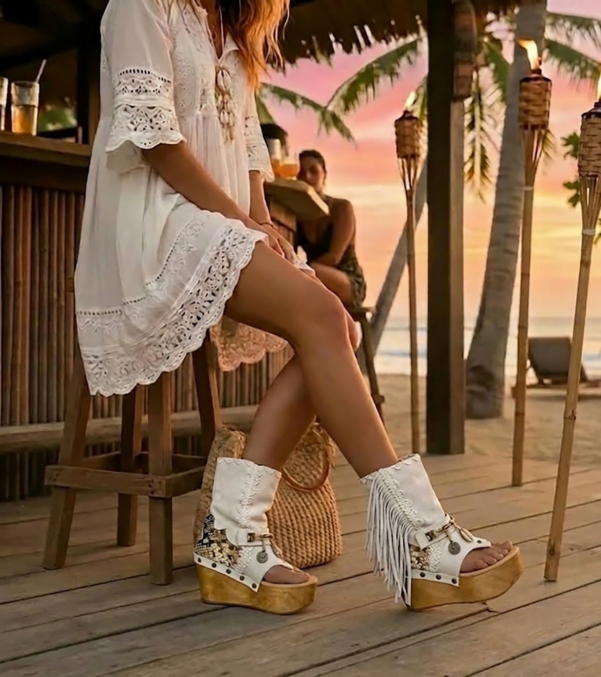 Boho-chic model at a beach club wearing Atenea White suede platform boots, showcasing the white fringe and artisanal details in a sunny, seaside atmosphere.