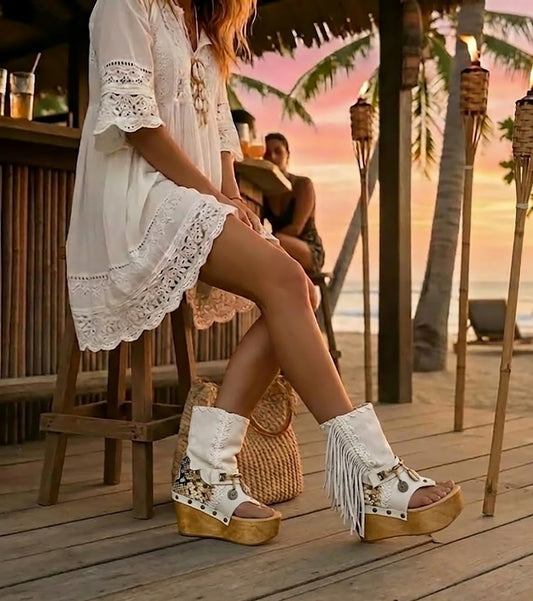 Boho-chic model at a beach club wearing Atenea White suede platform boots, showcasing the white fringe and artisanal details in a sunny, seaside atmosphere.
