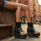 Model wearing Sol Caleyo Texas artisan sandals. High-end platform footwear in black leather with silver hardware and studded details. Luxury handmade wooden wedge sandals for a bold bohemian look.