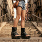 Model wearing Sol Caleyo Texas artisan sandals. High-end platform footwear in black leather with silver hardware and studded details. Luxury handmade wooden wedge sandals for a bold bohemian look.
