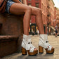 Model wearing Sol Caleyo bohemian leather platform sandals with wooden heel and silver decorative studs. High-end boho-chic summer outfit featuring artisan handcrafted footwear.