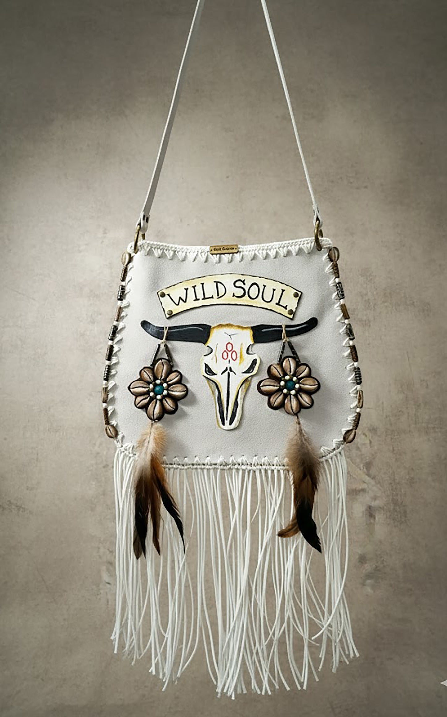 Handcrafted suede leather bohemian bag with a hand-painted and embroidered buffalo head design, decorated with natural shells, feathers, horns, fringe, an adjustable leather strap, and a fully lined interior.