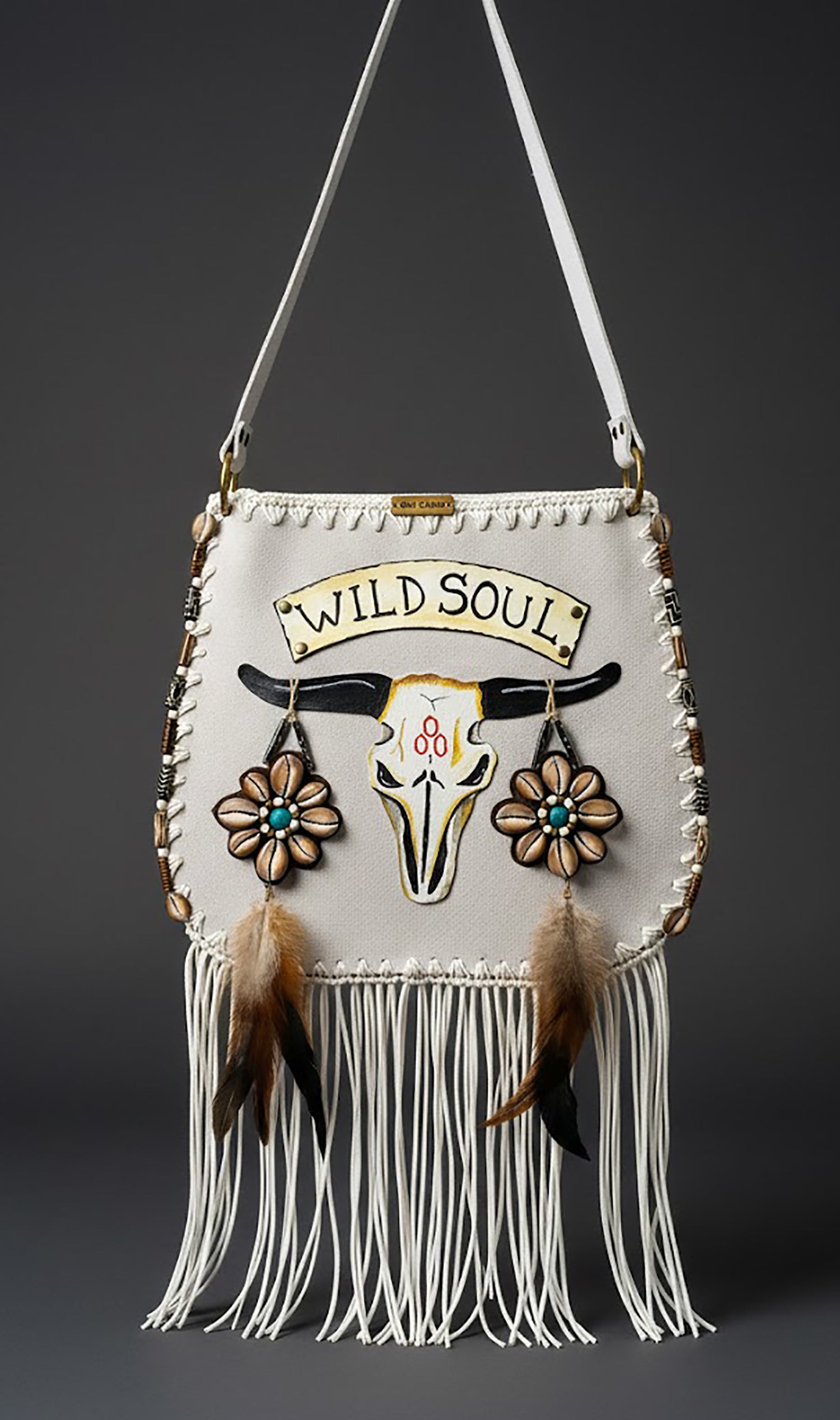 Handcrafted suede leather bohemian bag with a hand-painted and embroidered buffalo head design, decorated with natural shells, feathers, horns, fringe, an adjustable leather strap, and a fully lined interior.