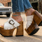 Detailed side profile of white leather Western platform clogs by Sol Caleyo, showcasing the 17 cm hand-carved wooden heel, antique-brass buckle, and rugged rubber outsole.