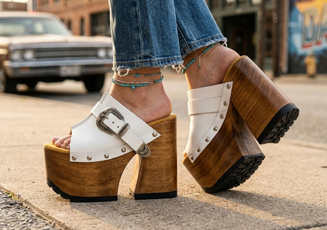 Detailed side profile of white leather Western platform clogs by Sol Caleyo, showcasing the 17 cm hand-carved wooden heel, antique-brass buckle, and rugged rubber outsole.