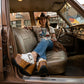 A woman in cowgirl attire wearing handmade white leather Western platform clogs by Sol Caleyo, sitting inside a vintage truck, showcasing artisan wooden heels and boho style.
