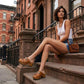 A woman sitting on New York brownstone steps wearing Sol Caleyo bohemian leather platform clogs and denim shorts.