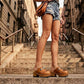 A woman sitting on New York brownstone steps wearing Sol Caleyo bohemian leather platform clogs and denim shorts.
