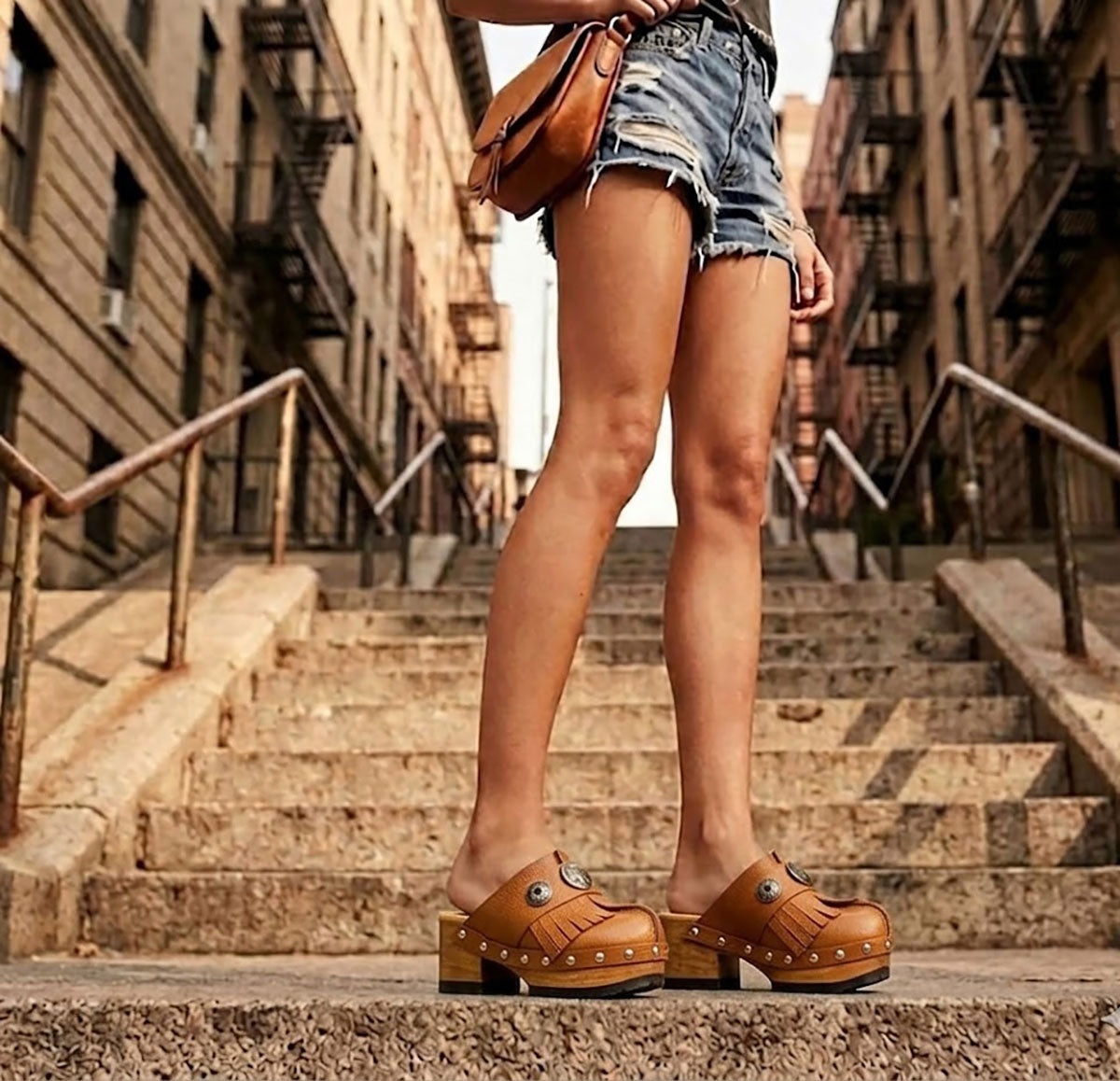 A woman sitting on New York brownstone steps wearing Sol Caleyo bohemian leather platform clogs and denim shorts.