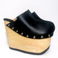 Handmade smooth black leather closed-toe wedge mule clogs with round flat silver studs and 15 cm light natural lacquered wooden wedge by Sol Caleyo.