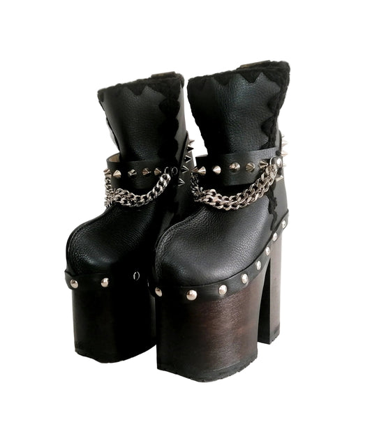 Handmade smooth black leather closed-toe platform ankle boots with silver pyramid studs, front chains and 15 cm wenge lacquered wooden heel by Sol Caleyo.