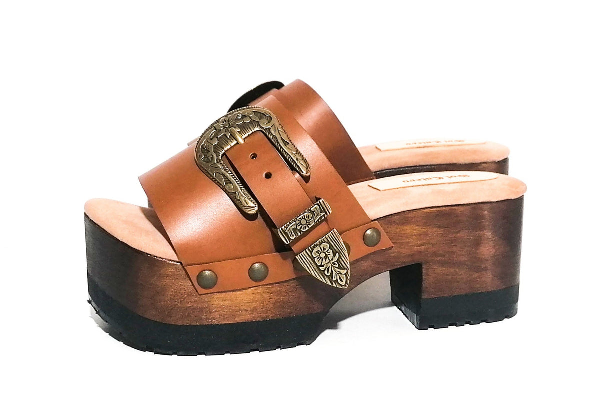 Handmade camel leather open toe platform mule sandals with wide strap, carved old-gold floral buckle, gold studs and 7 cm straight dark oak lacquered wooden heel by Sol Caleyo.