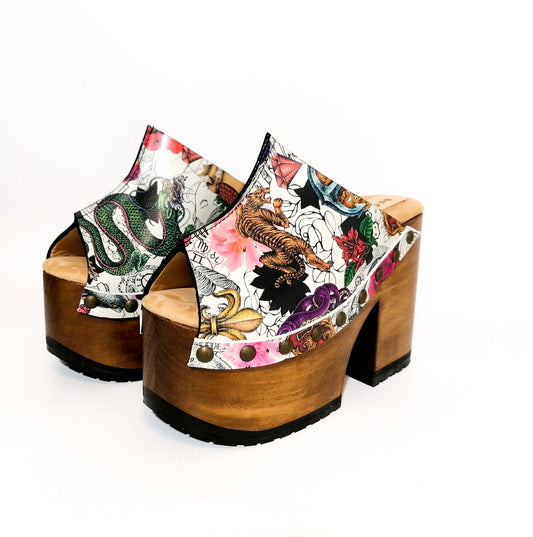 Handmade white tattoo print leather open toe platform mule clogs with tiger, dragon and floral print, wide strap, old-gold studs and 12 cm light oak lacquered wooden heel by Sol Caleyo.